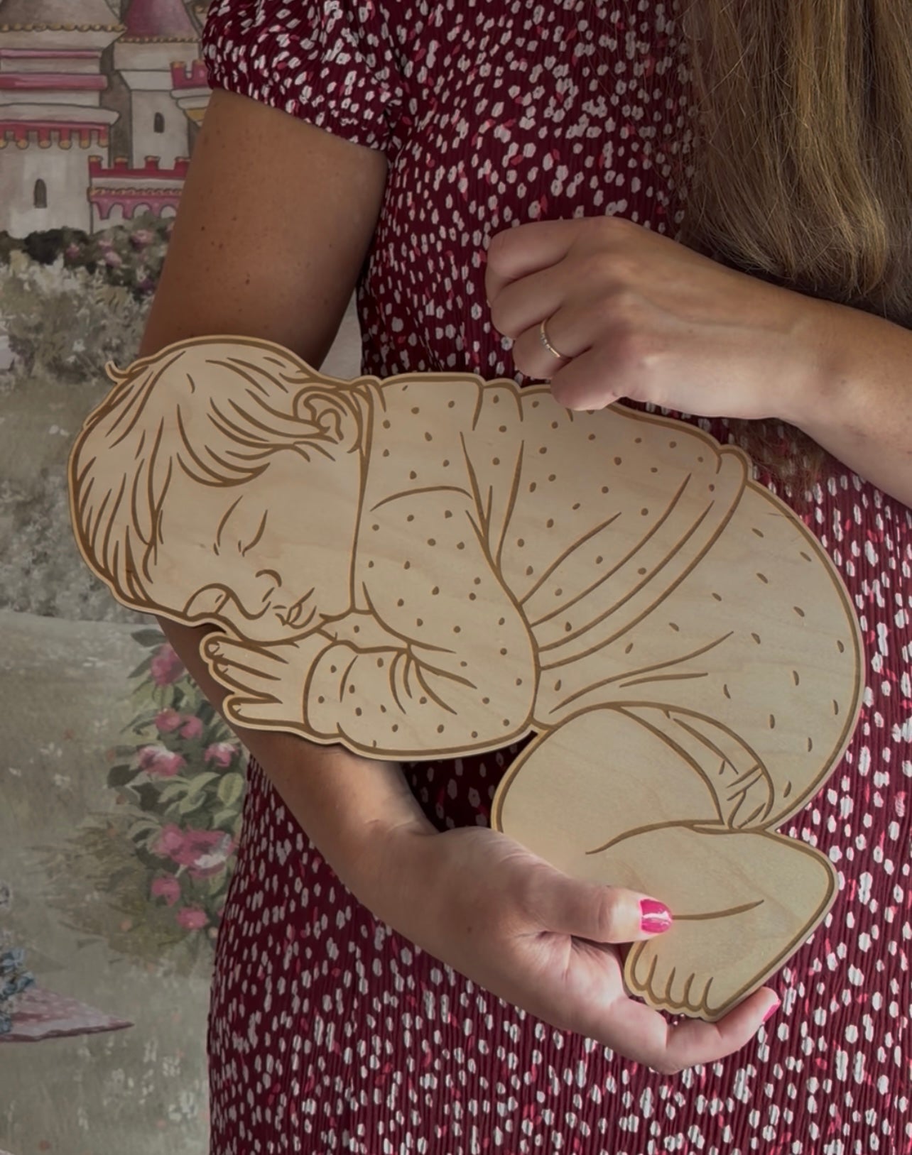 Vrouw houdt houten baby op ware grootte vast, met gegraveerde lijntekening van slapende baby